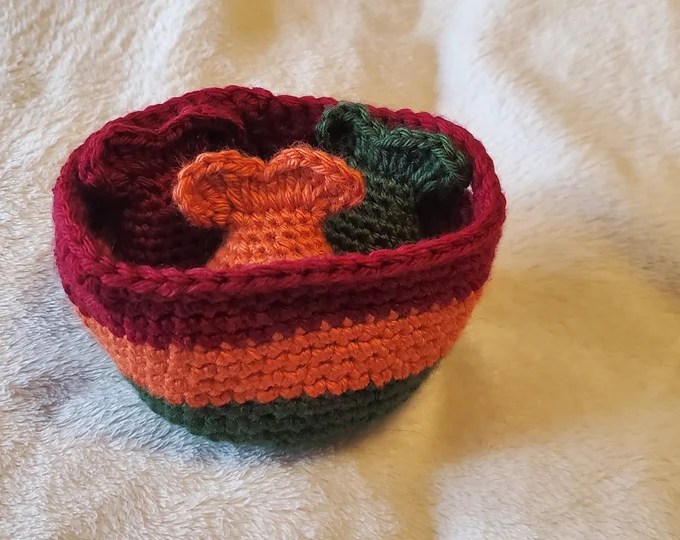 a picture of a crochet basket in the colors green, orange, and red with 3 crochet fish inside, one of each color that the basket is made of